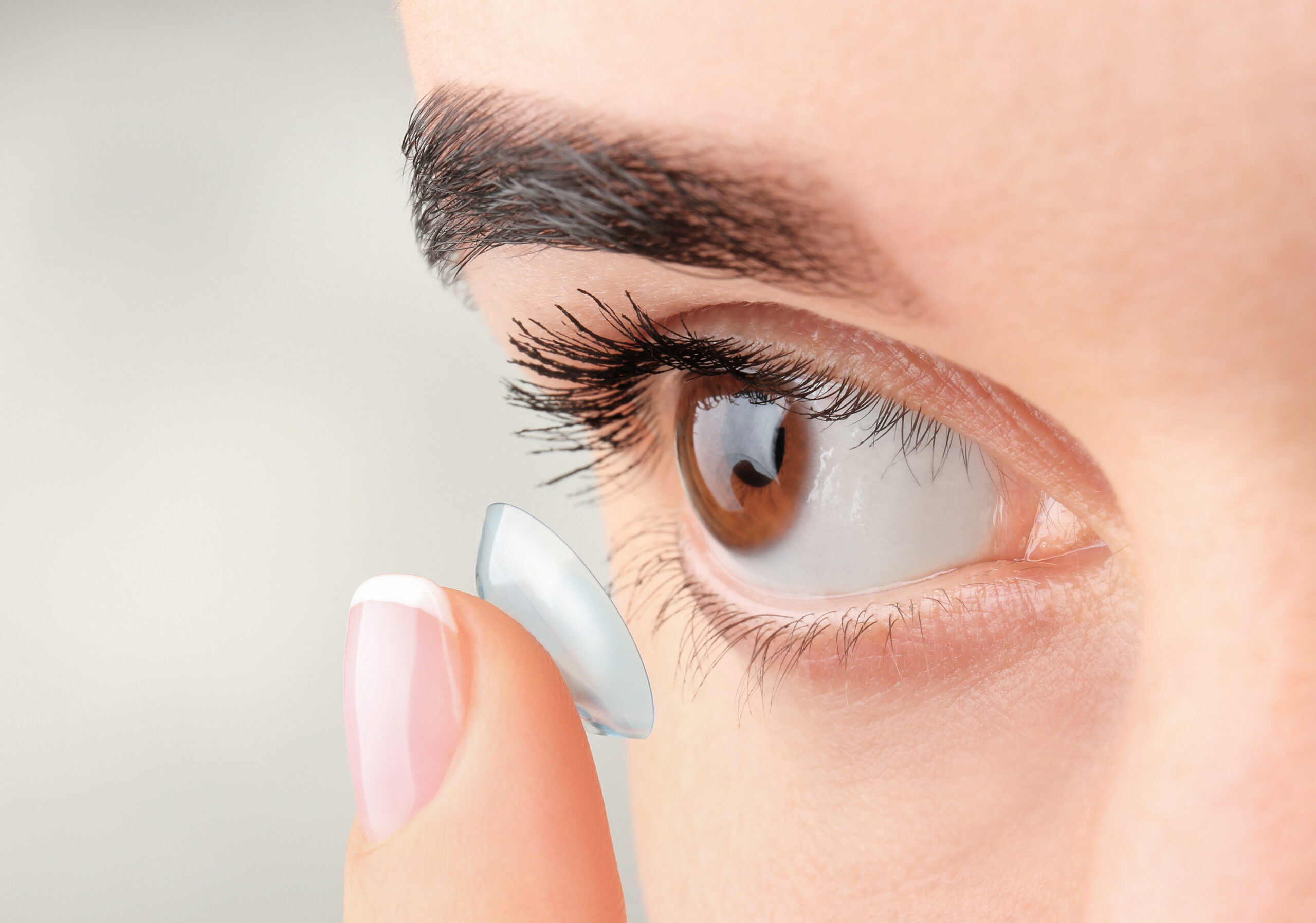 Young woman putting contact lens on light background, closeup